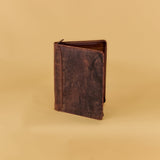 A dark brown distressed leather passport cover or small wallet standing upright on a warm beige studio background.