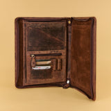 An open dark brown leather wallet or document holder with multiple interior pockets, shown against a solid beige background.