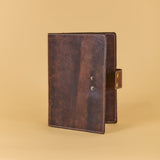 A dark brown distressed leather journal or planner cover standing upright on a warm beige background.
