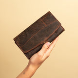 A hand holds the Leather Ladies Wallet Alice by Vintage Leather Sydney, a worn, waxed brown trifold wallet, against a plain beige background, highlighting its timeless vintage appeal.