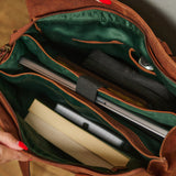 Close-up of an open brown leather bag showing a dark green interior organizer with compartments holding a laptop, notebook, and other accessories. A hand with red nail polish is visible holding the bag open.