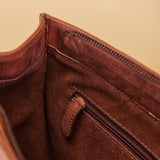 Close-up of the interior of a brown leather bag, showing a suede-like lining, zipper track, and a small leather pull tab.
