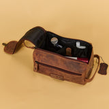 A brown distressed leather travel toiletry bag with an open zipper and interior organizer pockets, shown on a solid beige background.