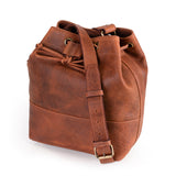 The Rosa Leather Crossbody Bag by Vintage Leather Sydney is shown on a white background, featuring brown leather with a drawstring closure, adjustable shoulder strap, and brass hardware.