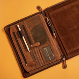 The Vintage Leather Sydney A4 Leather Compendium ACE, featuring multiple pockets, card slots, two pens, a zipper compartment, and business card display, is shown open on an orange background. Personalisation available.