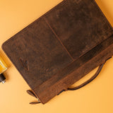 The A4 Leather Compendium - Cairo by Vintage Leather Sydney, featuring a handle and elegant brown leather design, rests on a yellow surface beside a yellow perfume bottle with a black cap.