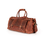 A brown distressed leather duffel bag with gold-tone hardware, featuring dual top handles, front flap pockets with buckle details, and a detachable shoulder strap, photographed on a clean white background.