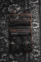 The Leather Hanging Toiletry Bag Rio by Vintage Leather Sydney, in brown and black, sits open on a patterned black and white rug, showcasing compartments filled with grooming items—an Italian-inspired example of elegance.