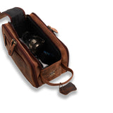 The Leather Travel Toiletry Bag Porter by Vintage Leather Sydney, shown open with a metallic item and accessories inside, features a handle and leather tag. The brown bag is set against a clean white background.