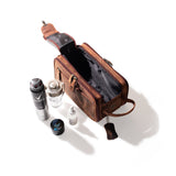 The Leather Travel Toiletry Bag Porter by Vintage Leather Sydney, in brown leather with an open zipper, sits on a white surface with a deodorant spray, glass bottle, small jar, and white bottle—ideal for storing travel essentials.