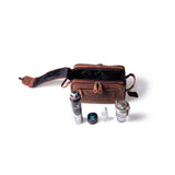 The Leather Travel Toiletry Bag Porter by Vintage Leather Sydney is open on a white background with essentials in front: shaving gel, a small jar, eye drops, and a metal-handled cup.