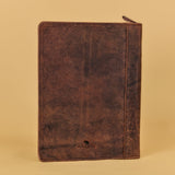 A dark brown distressed leather zippered document holder or portfolio standing upright against a solid beige background.