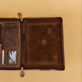 An open brown leather organizer pouch or document holder, laid flat on a warm beige background. The left side features multiple card slots, a vertical zip pocket, and a small clear ID window, while the right side is a smooth leather panel.
