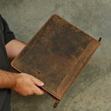 A person holding a distressed, vintage-style brown leather folio or binder cover against a textured gray background.