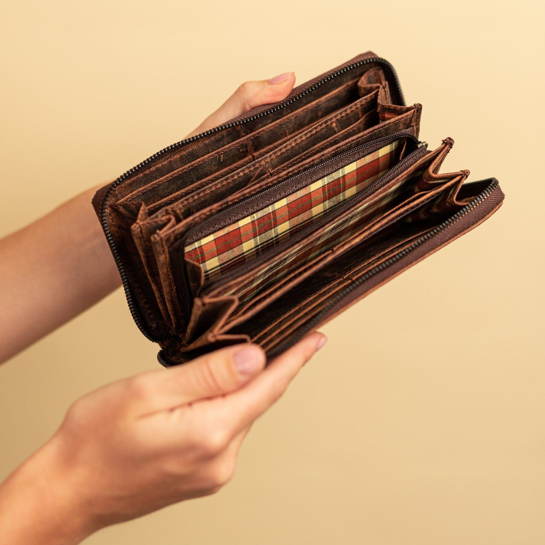 A person holds an open Womens Leather Zip Around Wallet Candice by Vintage Leather Sydney, showing multiple empty compartments and a plaid-patterned inner lining against a plain beige background.
