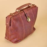 A brown distressed leather briefcase with brass hardware, shown from a three-quarters angle against a solid beige background.
