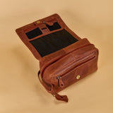 A brown leather travel pouch shown open, revealing a black interior lining and multiple compartments, set against a solid beige background.