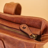 Close-up of a brown pebbled leather bag showing the interior lining, stitching, a gold-tone zipper, and a leather pull tab with a small black logo.