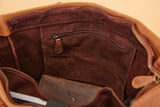 Close-up of the interior of a brown leather bag, showing a dark brown suede-like lining, a zippered pocket, and a matching brown leather insert or wallet.