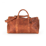 A brown distressed leather duffel bag with top handles, a detachable shoulder strap, and brass-tone hardware, photographed on a clean white background.