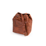 The Rosa Leather Bucket Bag by Vintage Leather Sydney is a brown leather drawstring bag with a long adjustable strap and brass hardware, displayed upright on a white background.