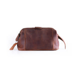 The Vintage Leather Sydney Leather Travel Toiletry Bag Manchester in brown, featuring a zipper and wrist strap, is ideal for makeup storage or as a travel grooming bag, shown against a plain white background.