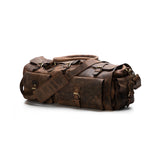 The Vintage Leather Shepherd is a spacious full-grain leather duffle bag featuring multiple buckles, pockets, and a shoulder strap, shown resting on a white background.