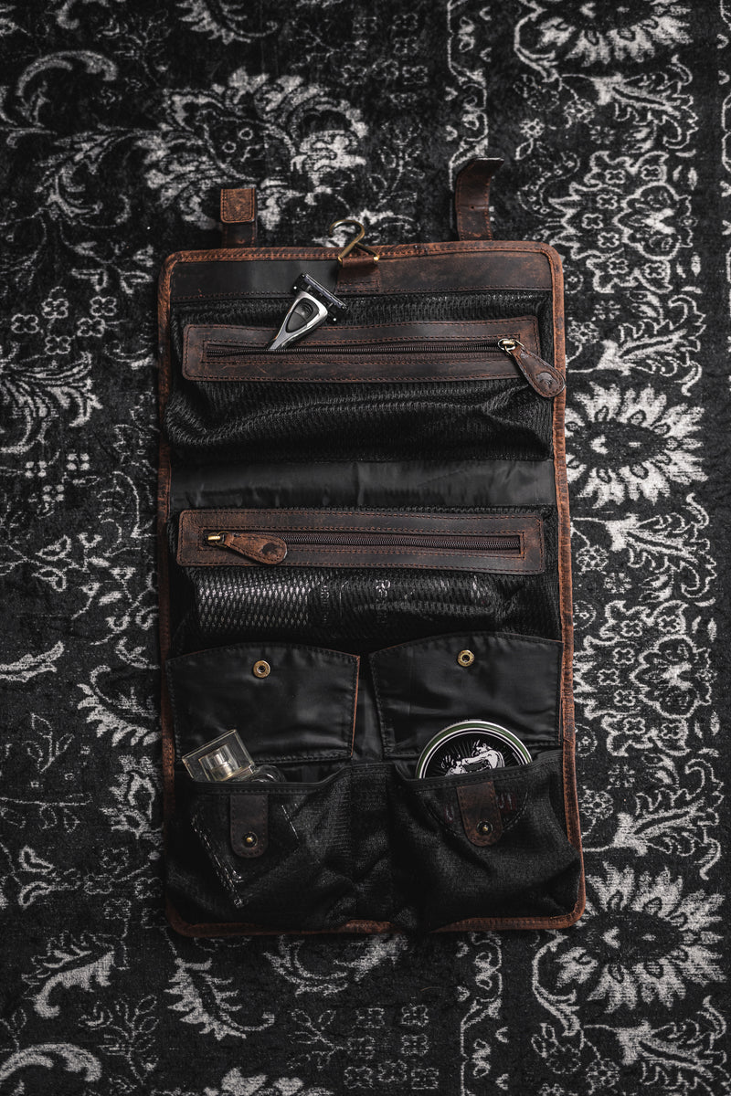 The Leather Hanging Toiletry Bag Rio by Vintage Leather Sydney, in brown and black, sits open on a patterned black and white rug, showcasing compartments filled with grooming items—an Italian-inspired example of elegance.