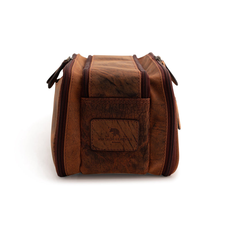 A brown Leather Travel Toiletry Bag Porter by Vintage Leather Sydney stands upright on a white background, featuring two zippered side compartments, a front pocket with an embossed logo, and is perfect for organizing toiletries when traveling.